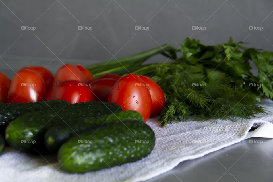 Fresh, bright, juicy vegetables and herbs for preparing salads and other vegetable dishes are on a gray, kitchen worktop.