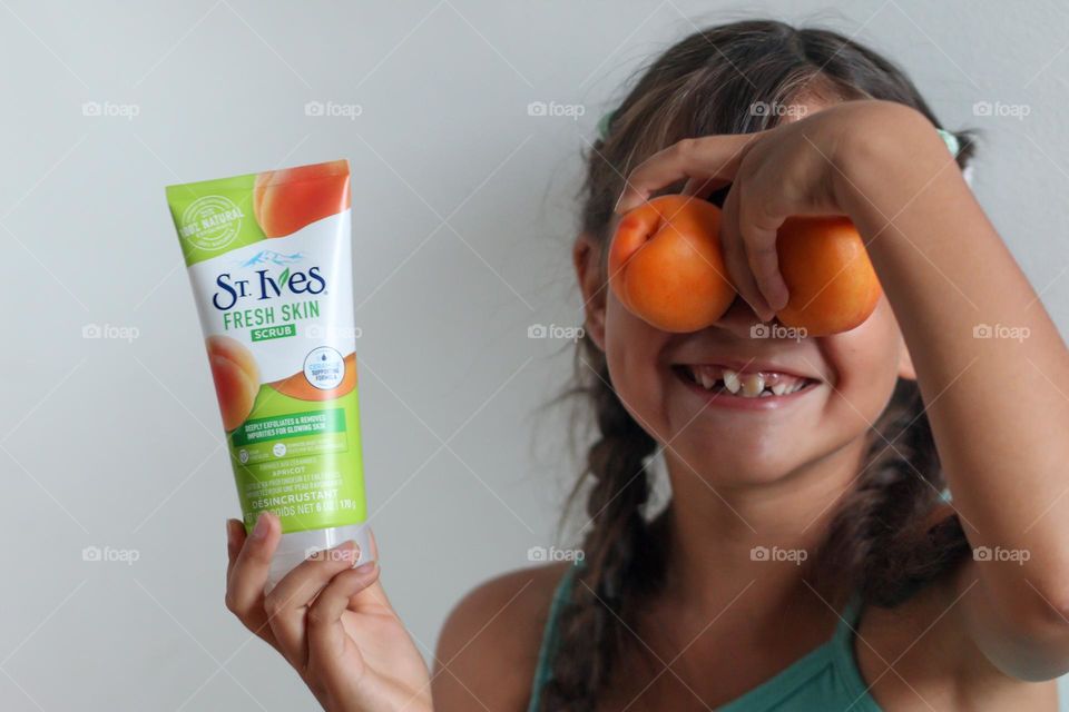 Cute girl is having fun with apricots and St.Ives body scrub