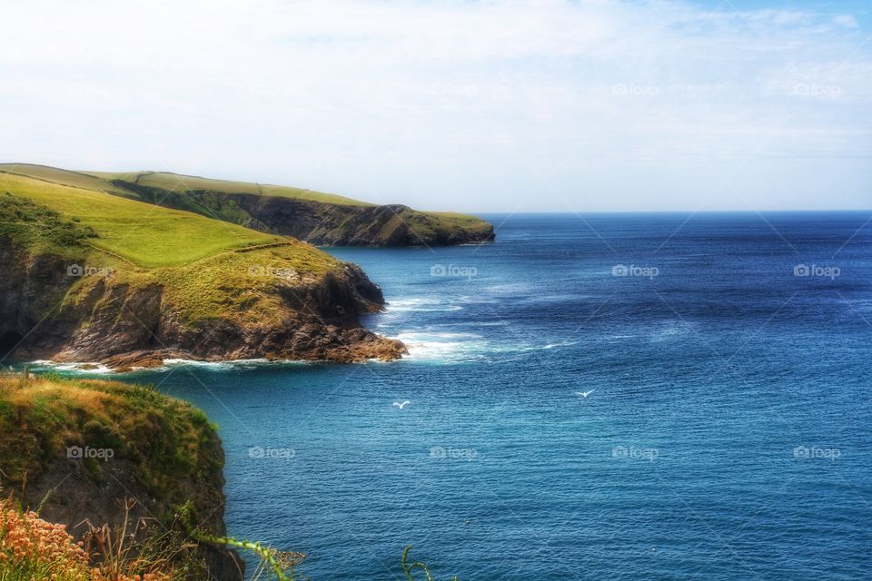 Green coastal cliffs above a calm blue ocean. Cornish cliffs sloping into the sea.