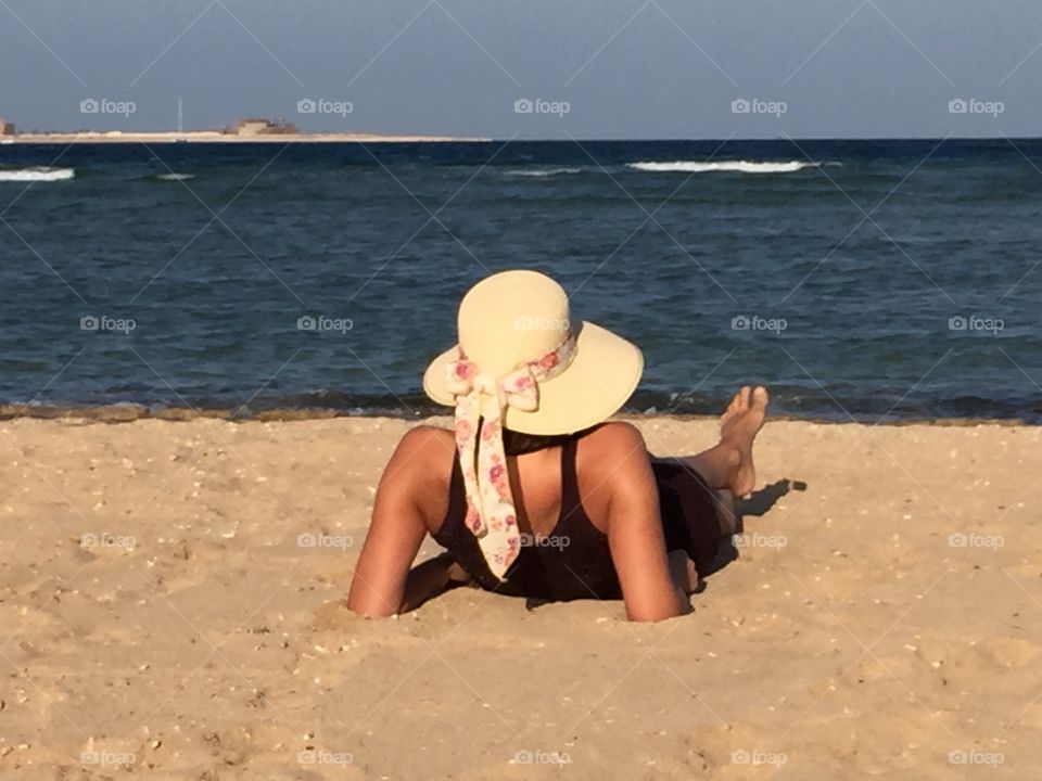 Woman with sun hat lying on the beach with sea view
