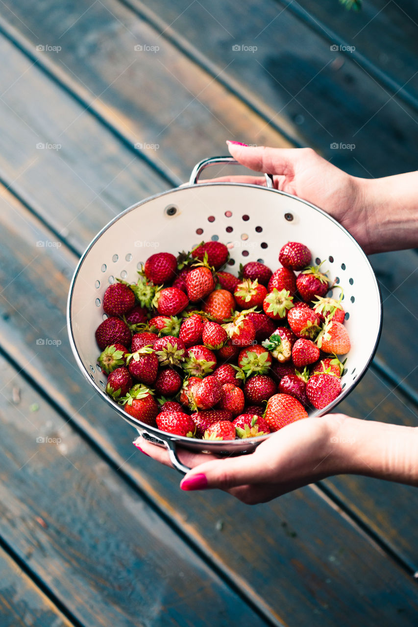 Female hand holding bowl of fresh strawberries sprinkled raindrops over wooden table