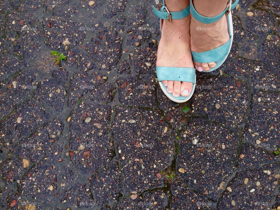 Feet in green sandals standing on road after rain