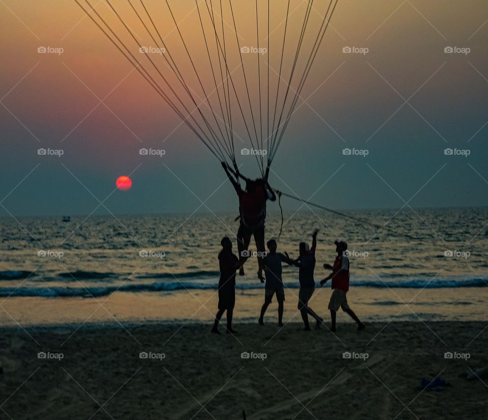 man descending off air balloon on the beach during sunset...