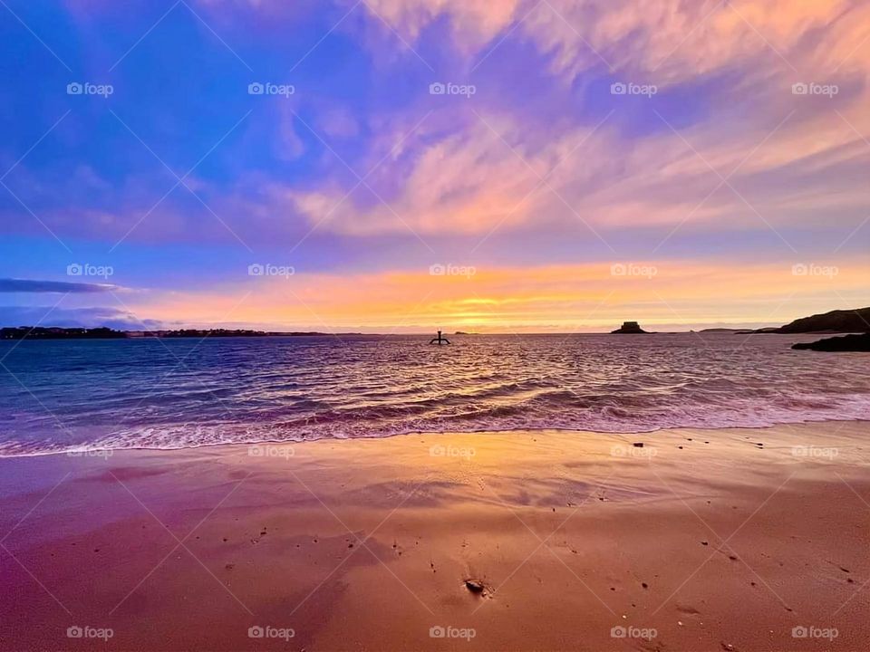 Sunset over the Bon secours beach and sea in St Malo with a cloudy sky showing a gradient of blue, orange and purple