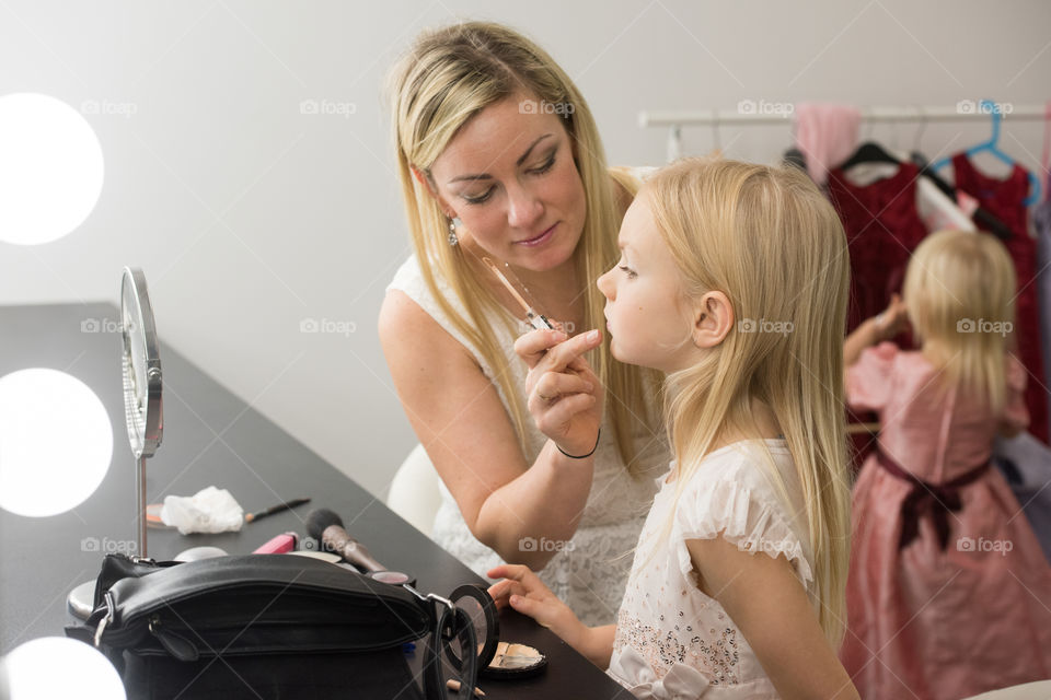 Young girl 6 years old trying out makeup, her mother is helping her.