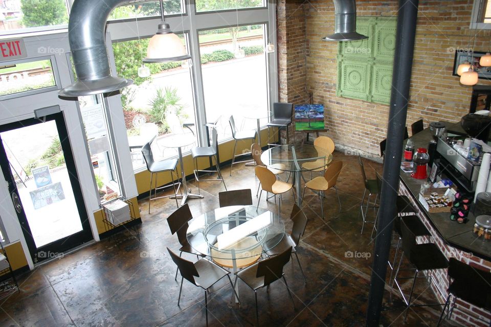 Bird’s eye view of coffee shop sitting area tables stools by floor to ceiling windows modern wall art