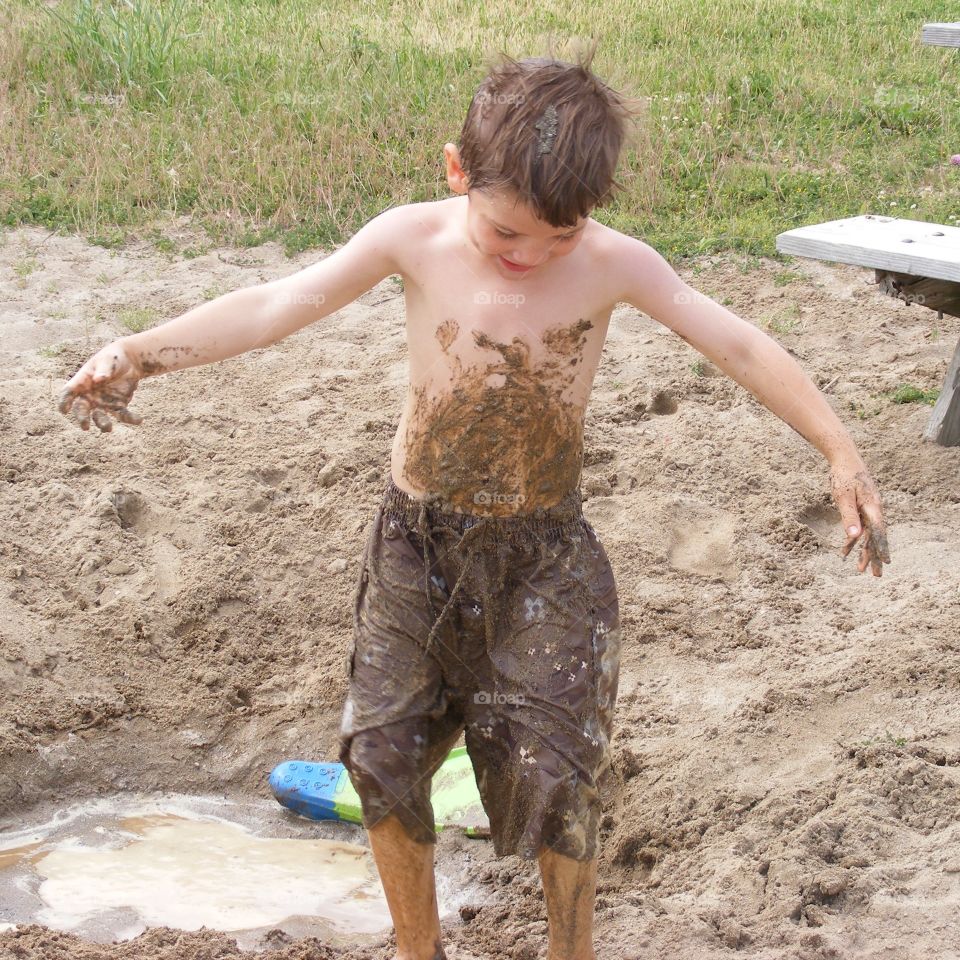 A dirty boy covered in muddy sand.