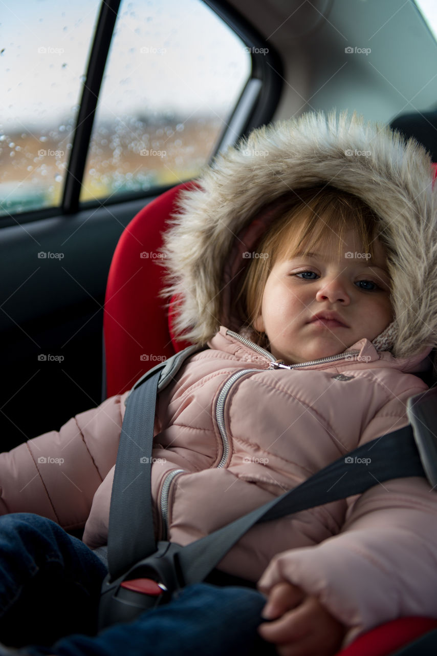 baby in her car seat wearing caot and a good in a rainy day