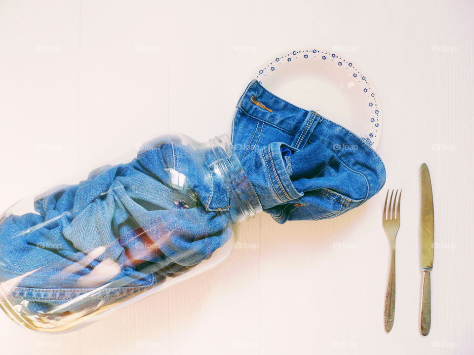 in a glass jar men's jeans pants and a plate with a fork and knife on a white background