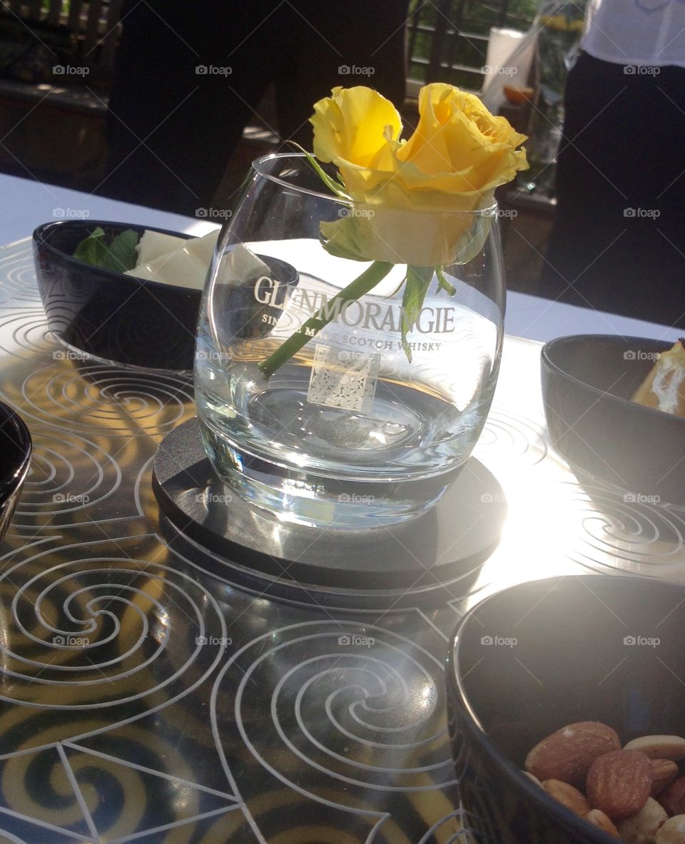 Whiskey glass with a yellow rose on a table