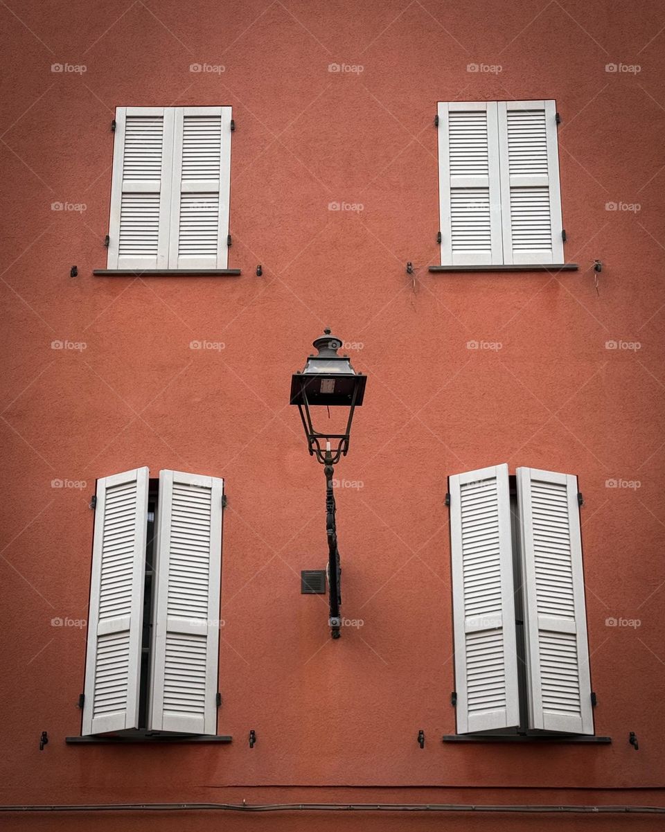 Symmetrical shot with white windows and old black vintage lantern, street in Italy, Parma 