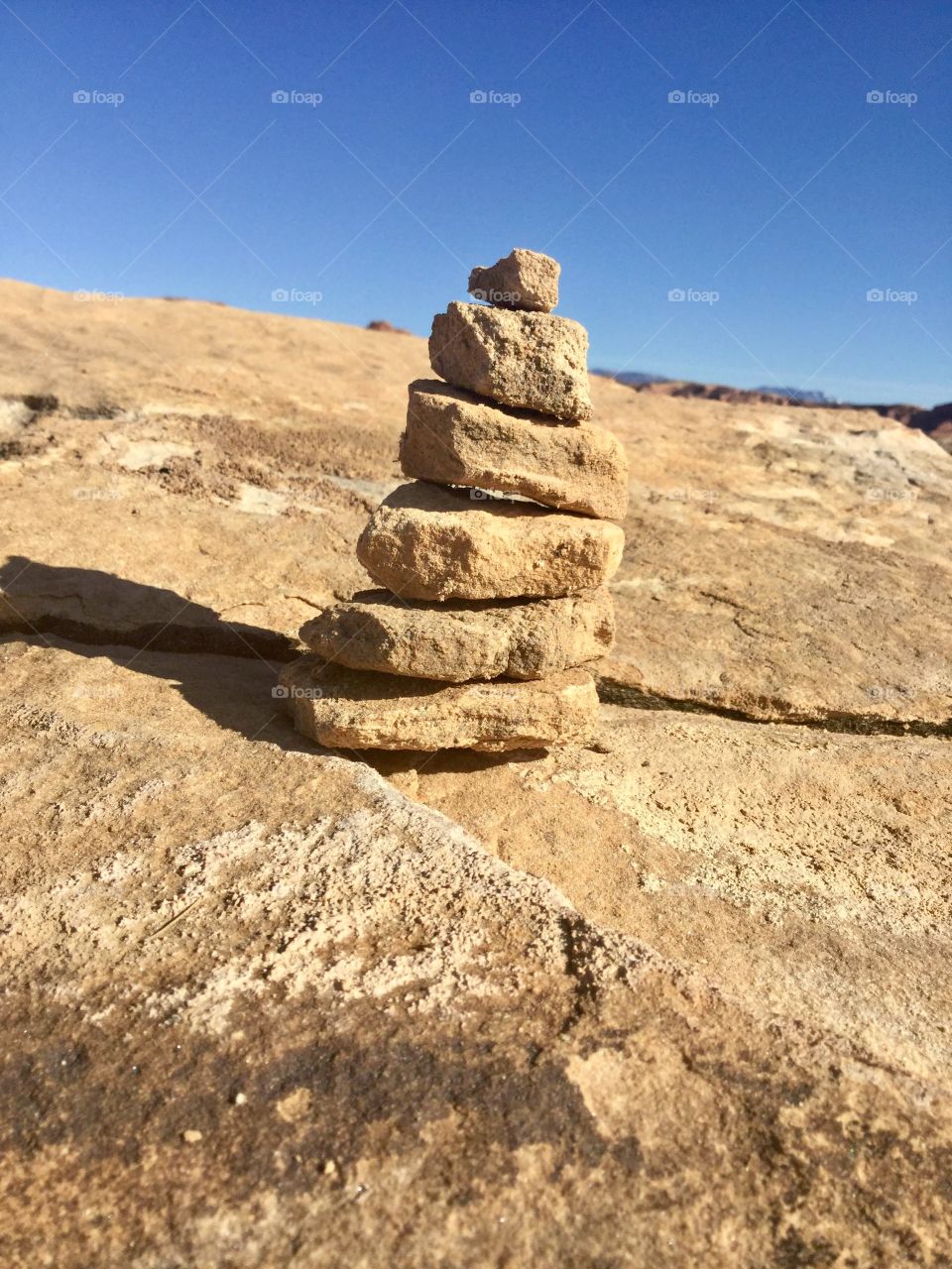 A simple tower of rocks with a bright blue sky behind. A clean shadow drops from the left side.  