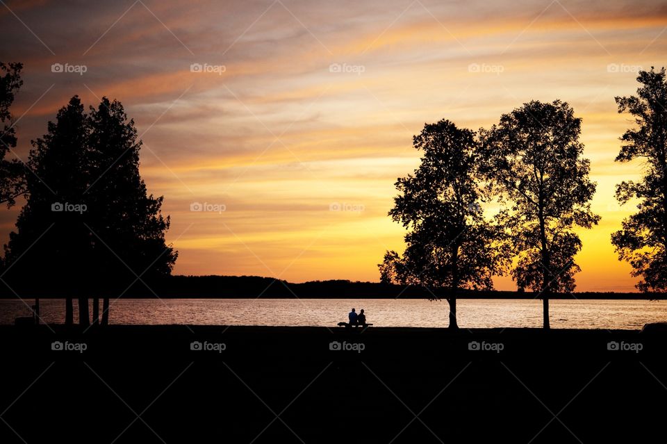 Couple sitting on a bench at a lake at sunset