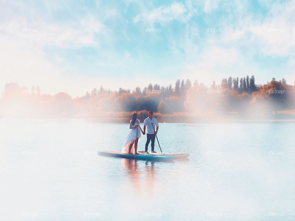 Young couple holding hands while standing on the paddle board in the middle of the lake 