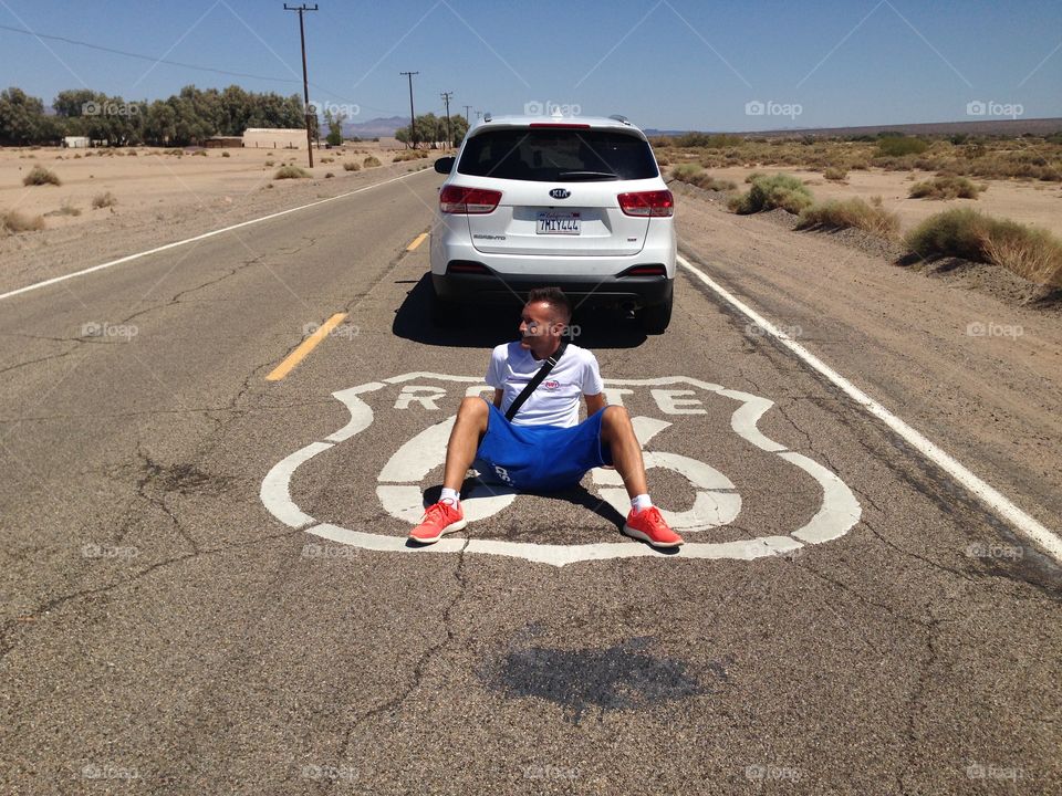 Man sitting on route 66 sign road with car