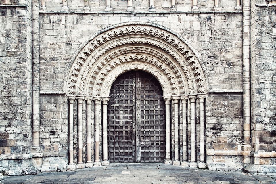The main doorway to Selby Abbey in Yorkshire. An ornate and elaborately carved doorway with stone masonry carvings and a heavy wooden door.