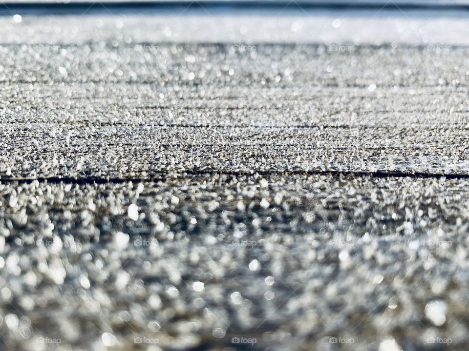 Low-angle view of ice crystals on wooden surface in sunlight 