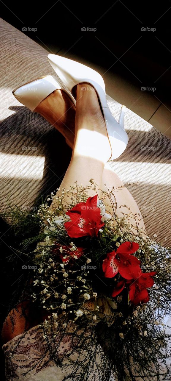 ramo de flores una piernas cruzadas y unos zapatos altos blancos