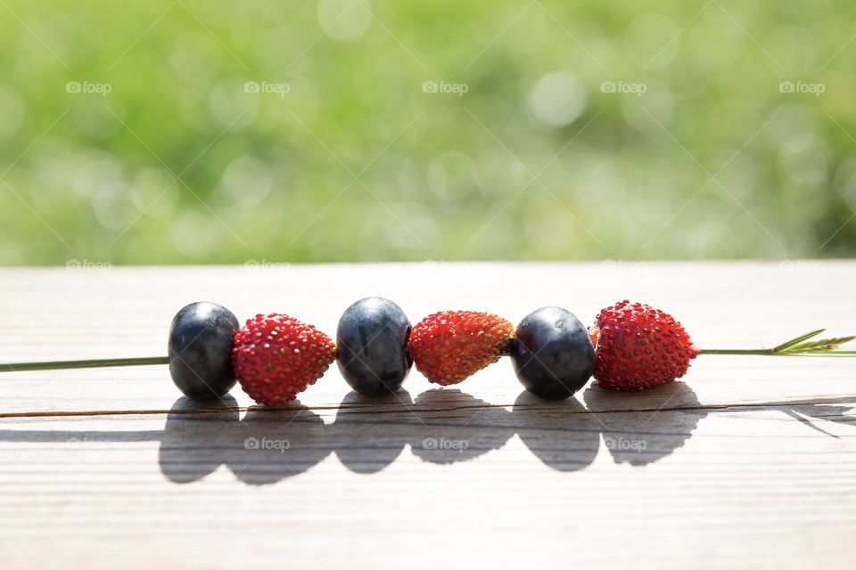 Colorful wild strawberries and blueberries on grass straw in bright sunlight 