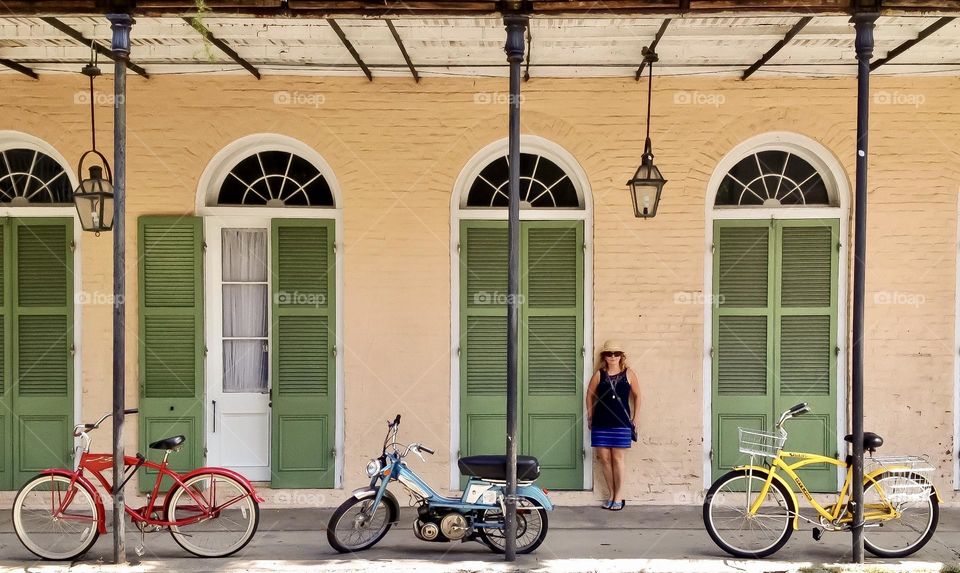 A beautiful woman poses beside storm shutters behind three bikes representing the primary colours.