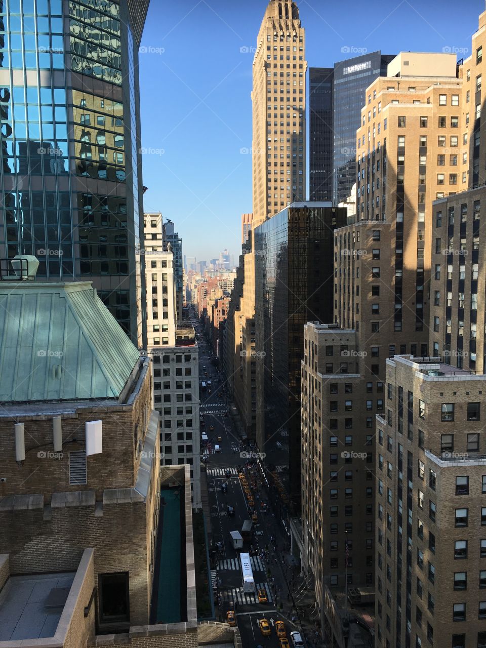Looking down a street from the birds eye view. Beautiful shot of gorgeous Manhattan taken from a balcony, making you feel like you are flying through the city. Reflections adds to the artistic element 