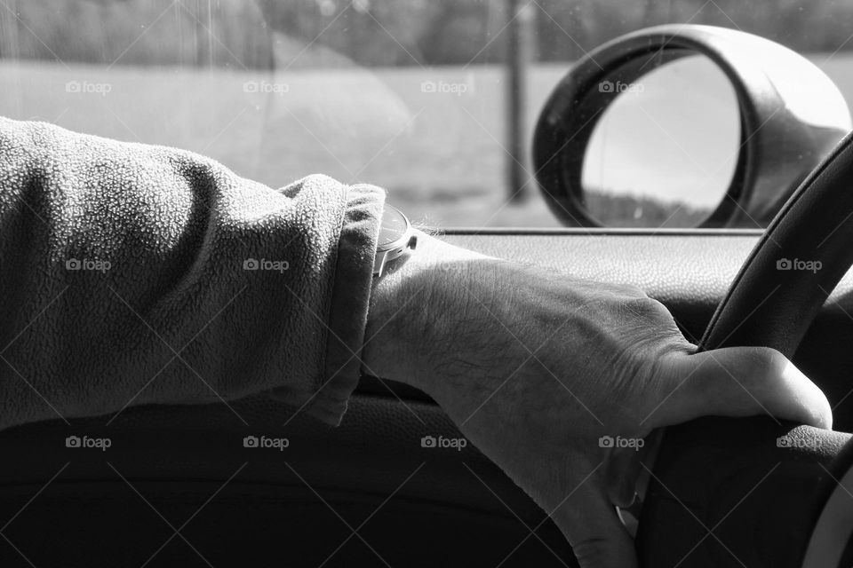 Close-up of a man's arm with a wristwatch on the steering wheel while driving