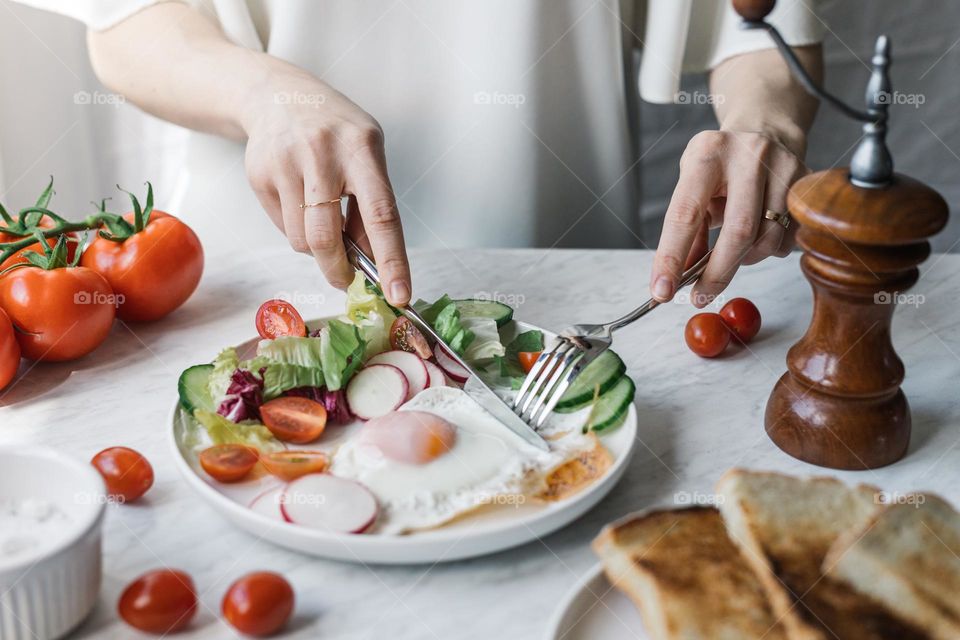 Woman eating a healthy breakfast with eggs, veggies and bread.