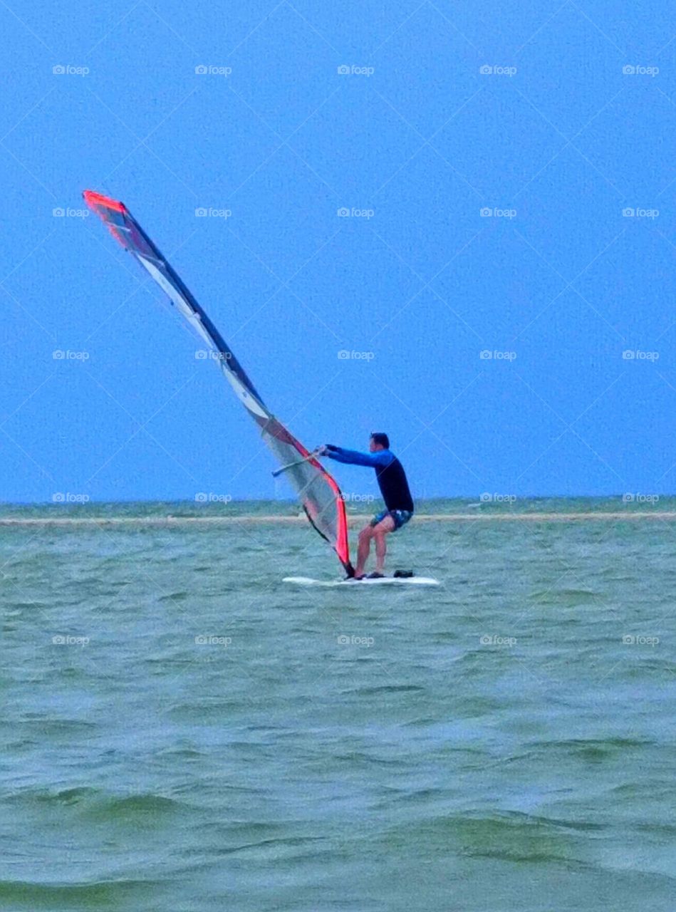 A man controls a sail on a surfboard in the sea against the background of water and sky.  Movement on water