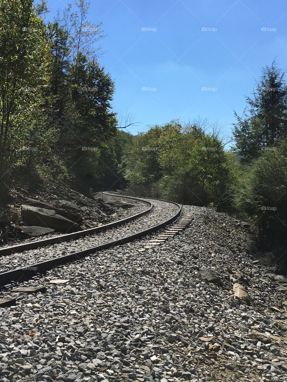 Rocks, train tracks, trees while viewing the unknown brand around the mountain. 