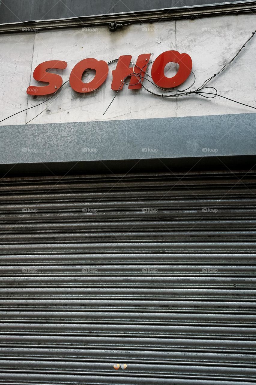 Metal shutters pulled down under a shop named Soho in red letters, haphazardly holding wires and cables 