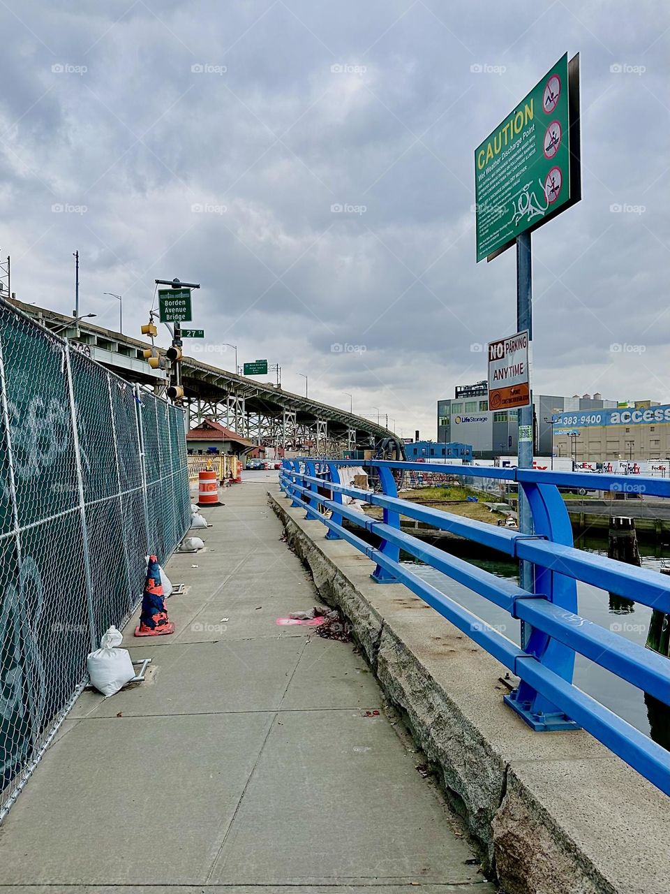 This is the „Borden Av Bridge“ at „Dutch Kills“ in LIC. The blue railing swerves elegantly into the distance while the green fence on the left is still. The curved trajectory of the „BQE“ above it puts a twist in space. 2023. Hypnotic Productions