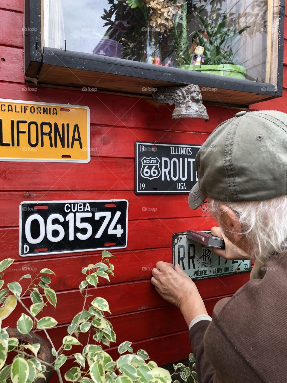 old man bracketing old car license plates on red painted wooden wall