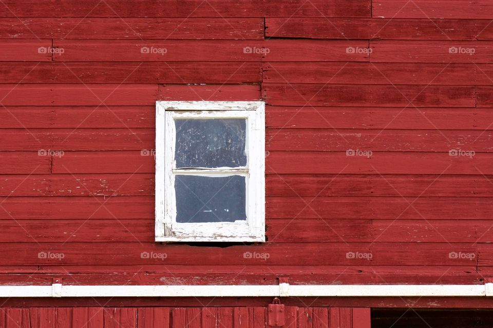 Minimalistic view of the side of a red barn with a small white-trimmed, double-hung window