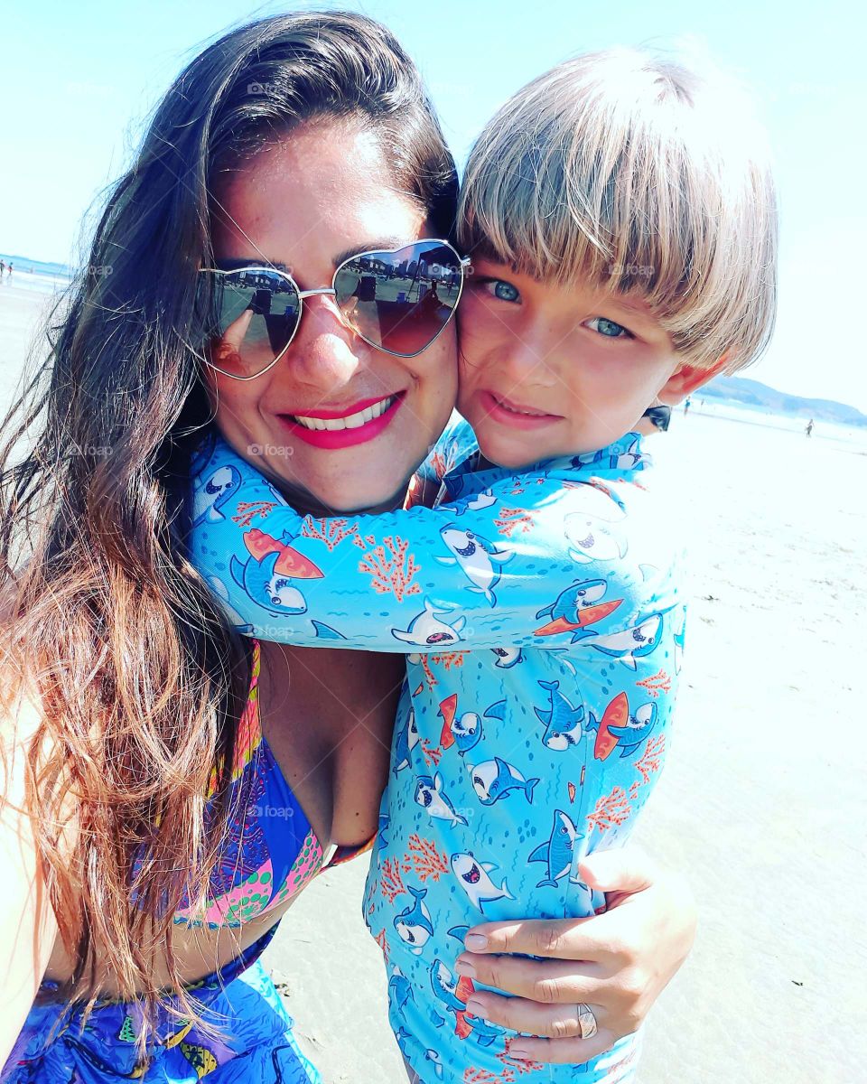 beautiful child cuddled with his mother on the beach enjoying the summer.