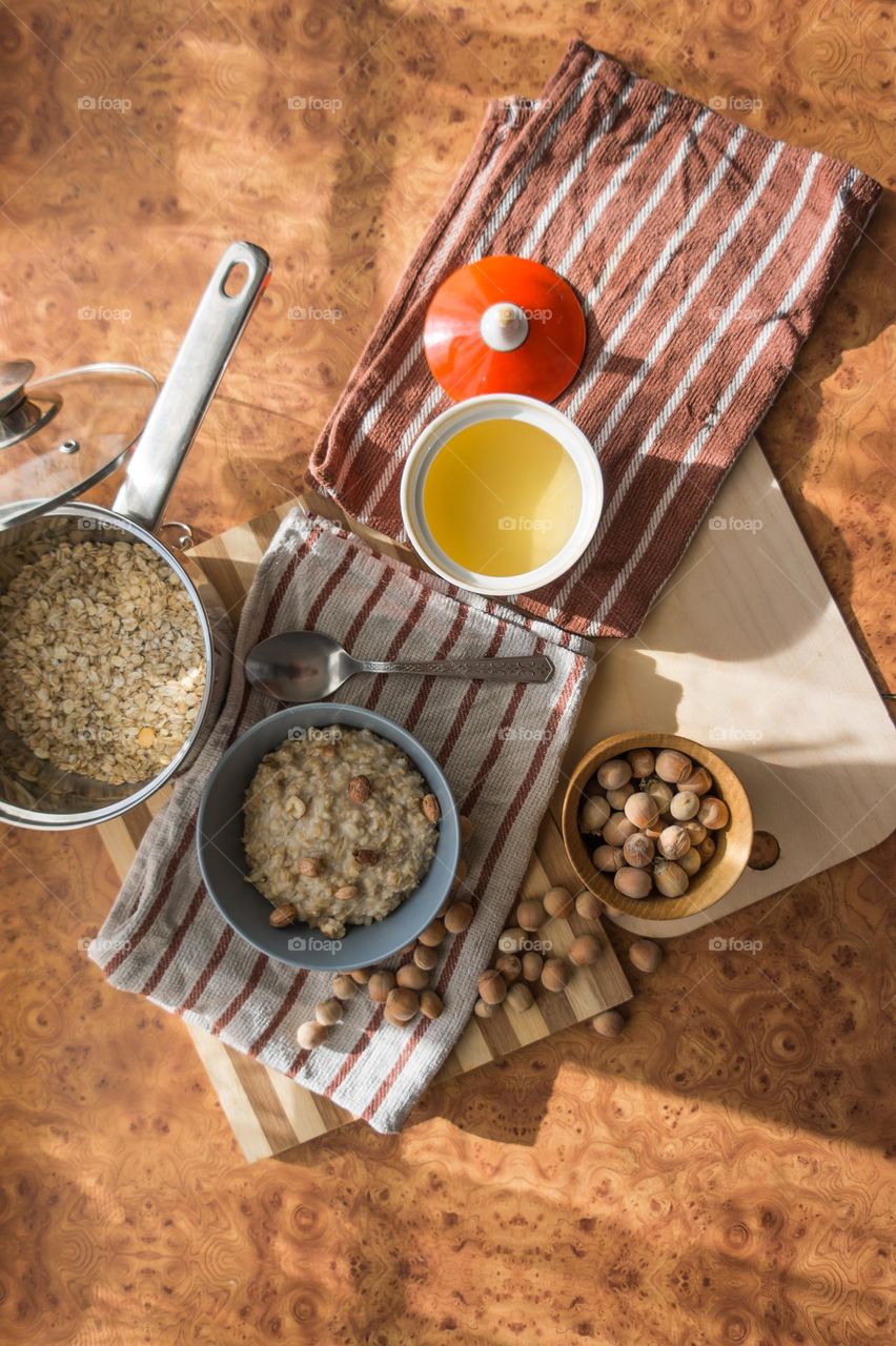 Cooked oatmeal in a deep gray plate with hazelnuts and honey.