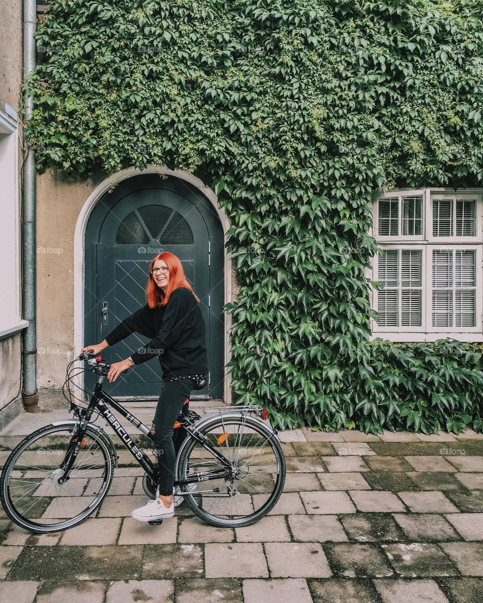 Happy woman riding bicycle in front of house decorated with vine