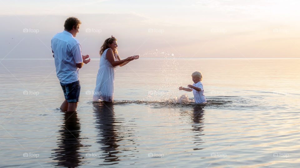 Young family with two kids splashing water at sea at sunset