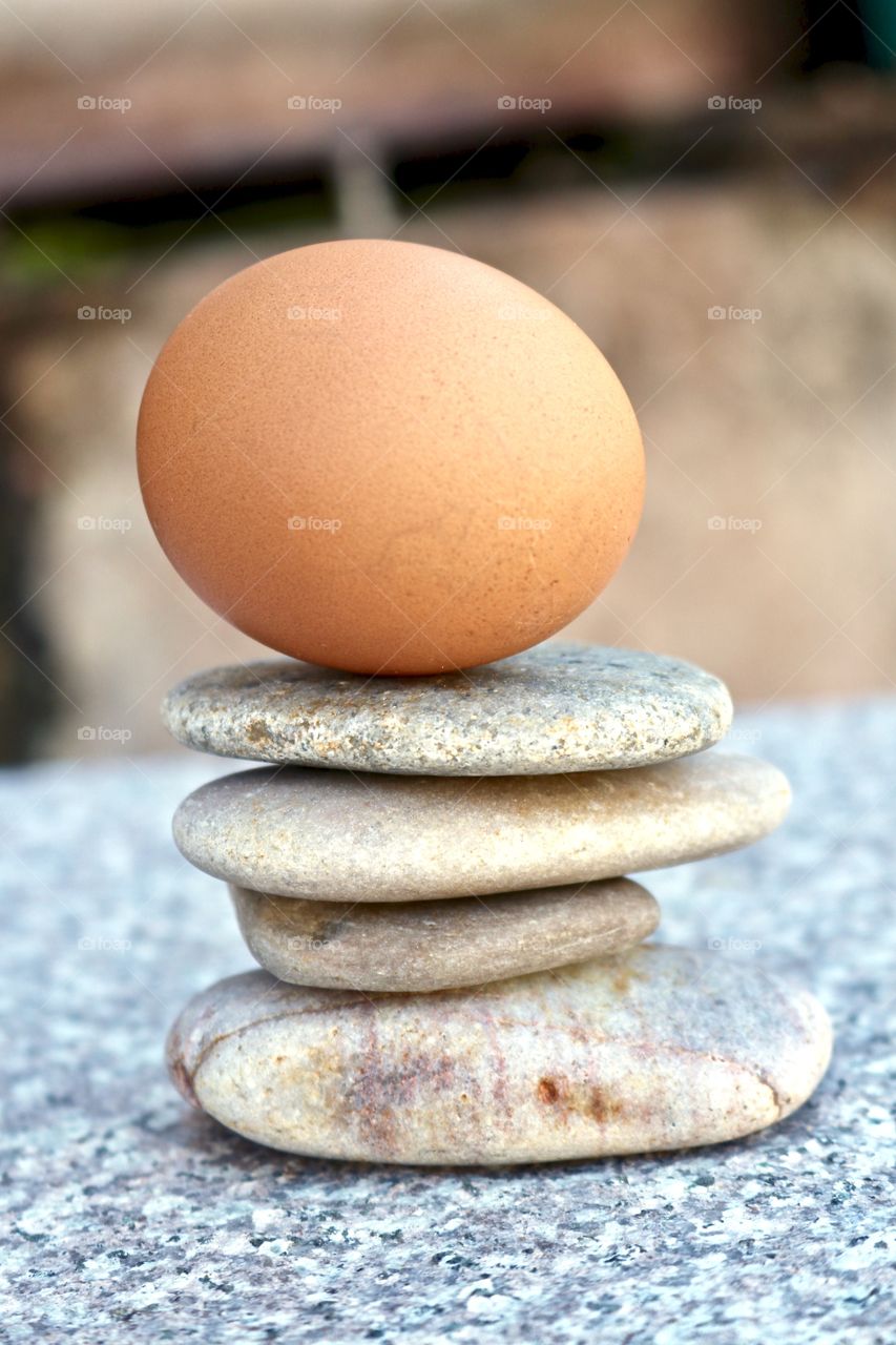 Brown egg balancing atop smooth stone rock stack on marble surface, concept life, business, ideas, creativity endurance or stability