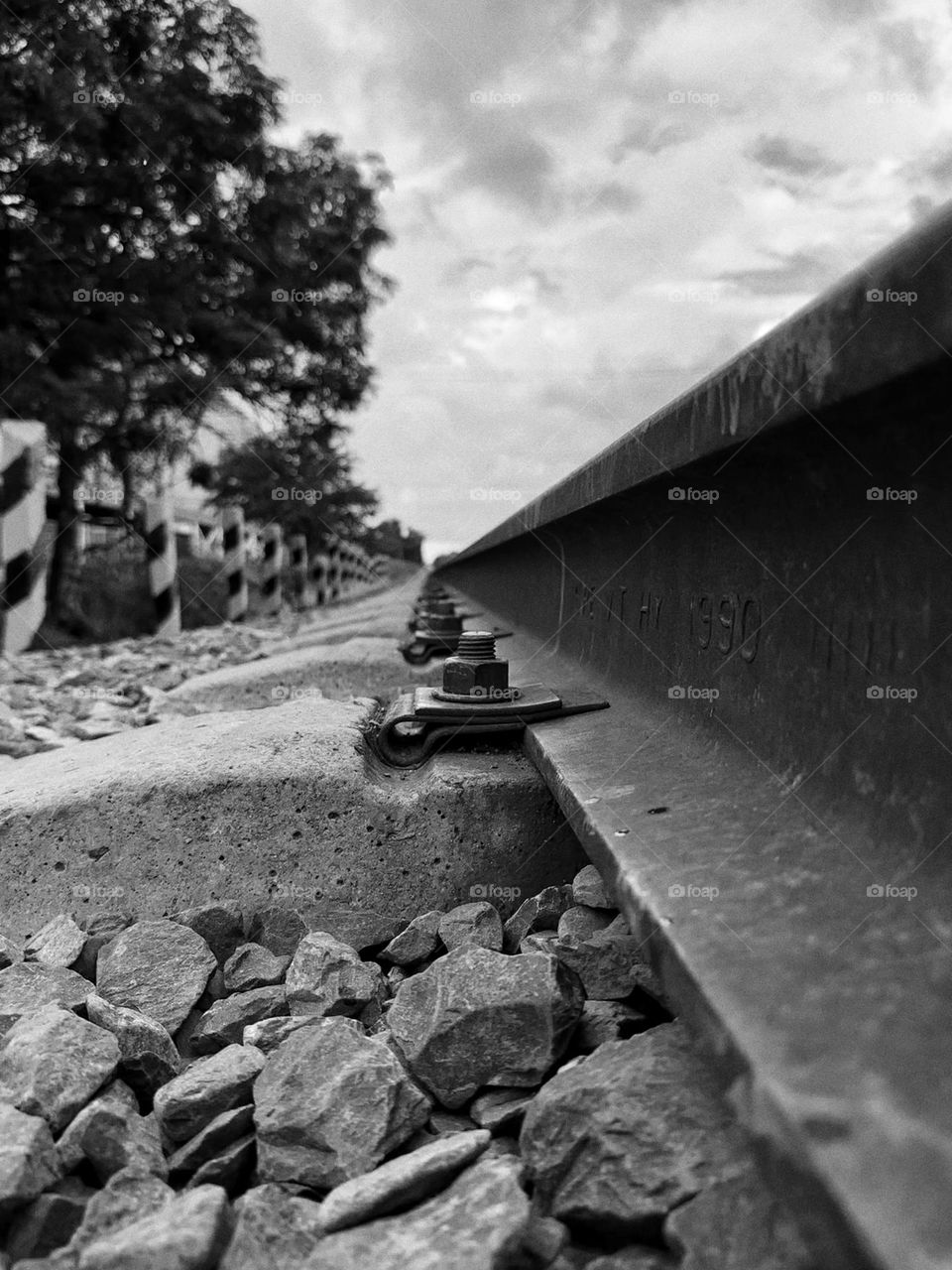 Old screws of a train tracks forming a pattern heading to the horizon of it with stripped poles and trees around.