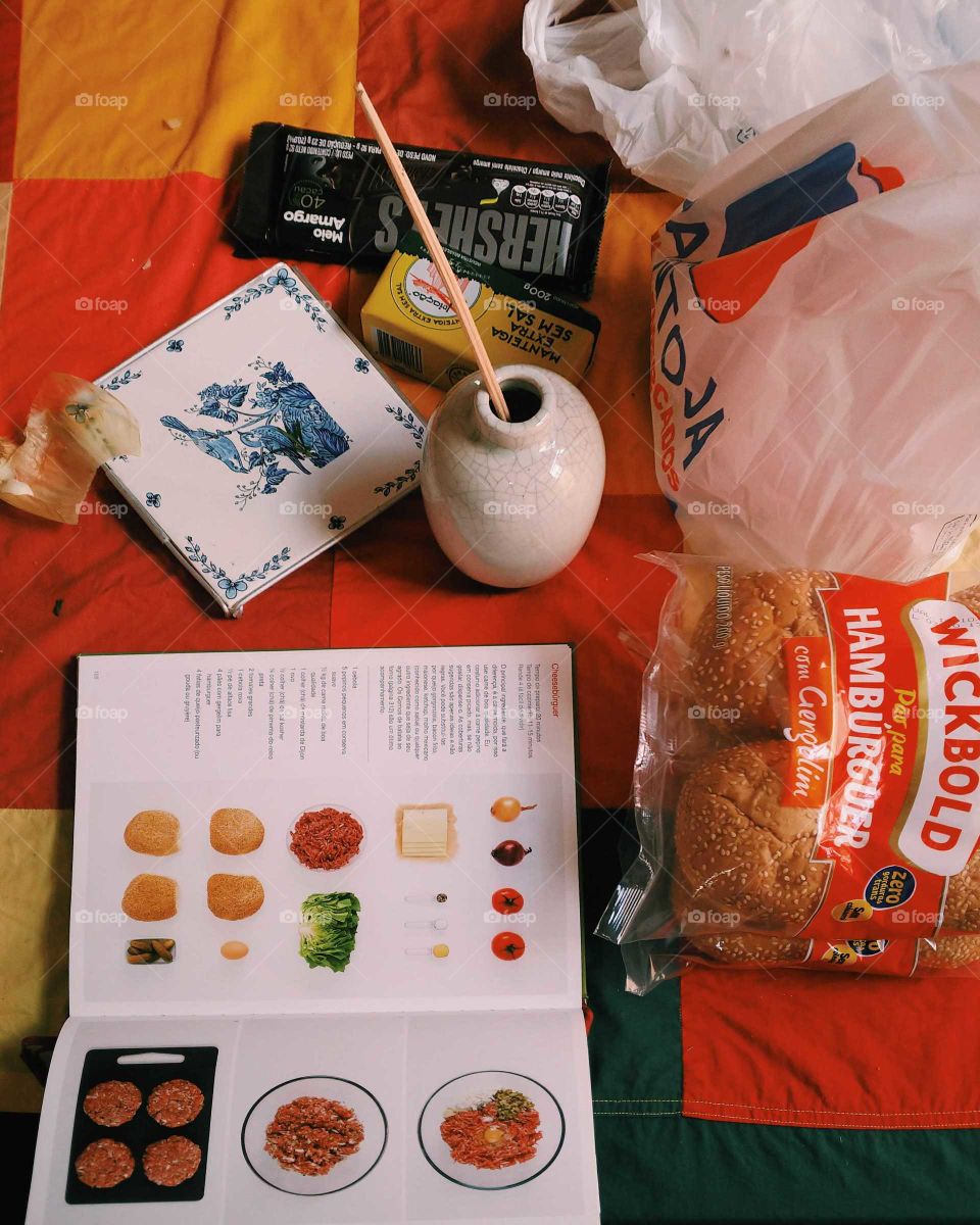 Picture of a table full of food and a recipe book, cooking table with hamburger buns, chocolate and onions