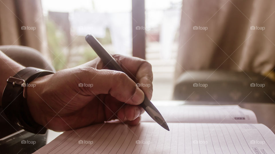 Closeup of man's hand working on a sheet of paper document with pen at desk. A businessman working on a financial report. Loan Tax Vat computation background concept. Copy space room for text.