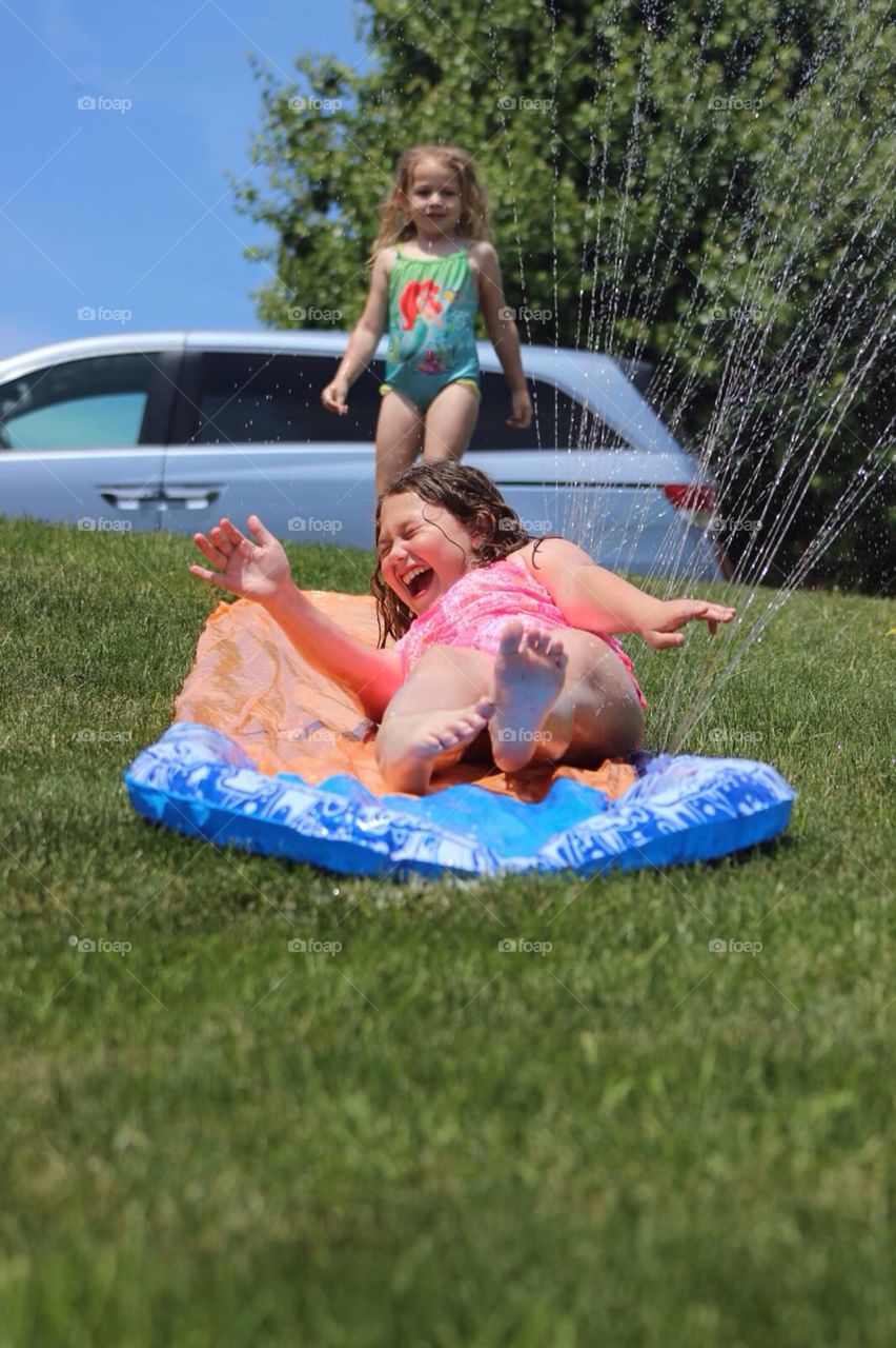 Sister having fun in garden near sprinkler