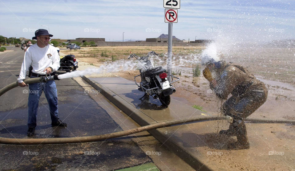 A motorcycle officer is sprayed down by a fellow officer to get the