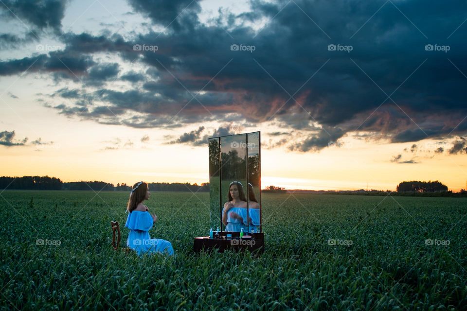 Young woman in the green field is looking in the mirror 