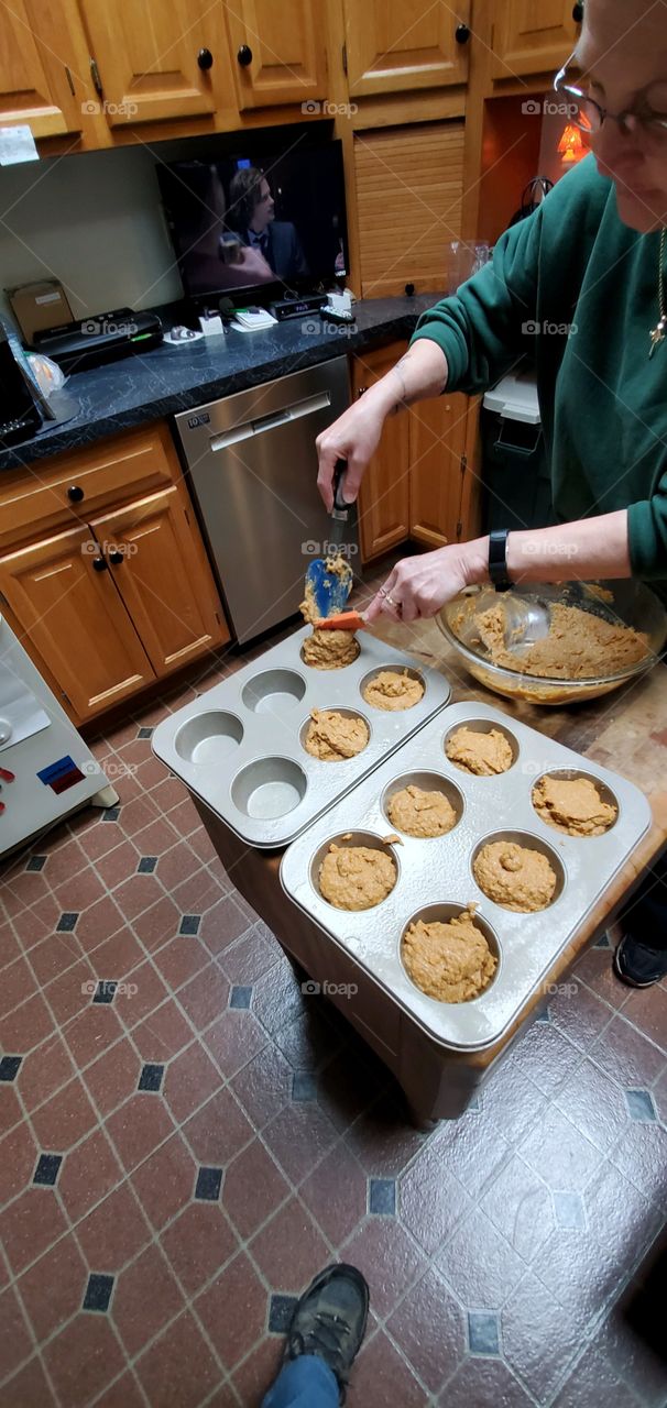 Baking today. Using spatulas, filling muffin pans with homemade batter into pans from glass bowl. ready for oven.