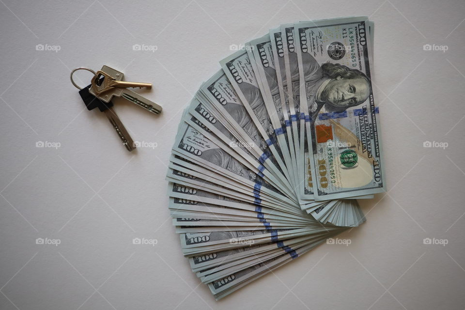 100 dollar bills on a white background with apartment keys. Pile of new one hundred dollar bills bills.