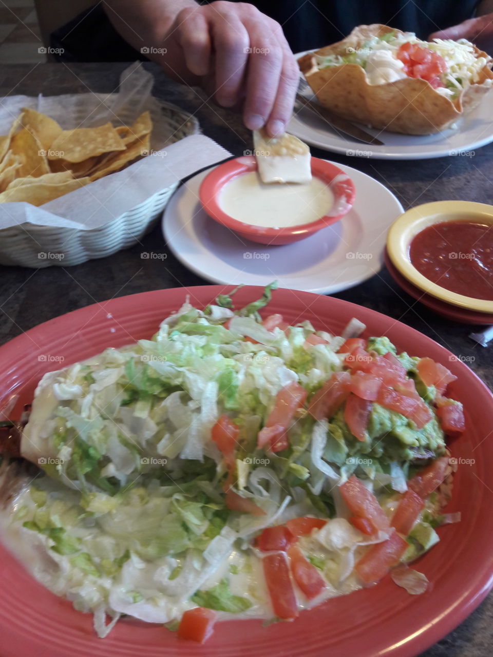 Person's hand dipping food in a dipper with salad in plate on table