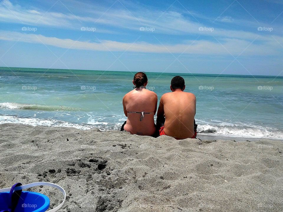 Cute couple sitting in the sand on the beach soaking up the sun enjoying the waves washing ashore on a beautiful summer day off the Gulf Coast of Florida.
