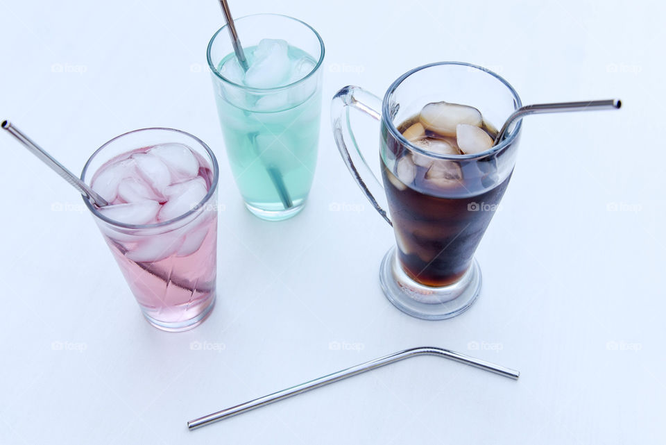 Three drinking glasses filled with ice and different colored liquids