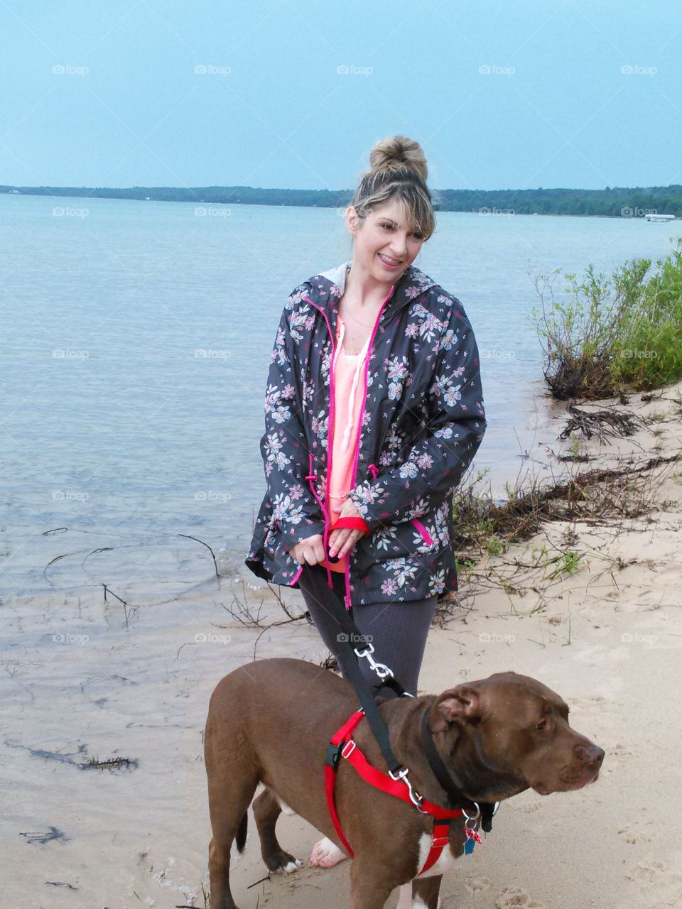 A girl and her dog. young woman on the beach with her dog, smiling at someone off camera, water background